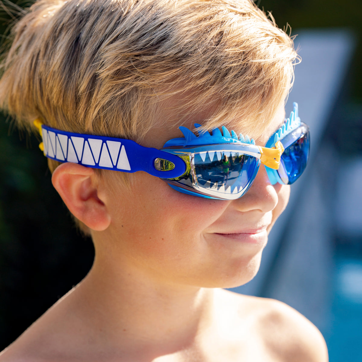 boy smiling wearing draco the dragon kids' swim goggles in blue dragon showing a silicone spiked gasket, sharp teeth printed lens and patterned strap
