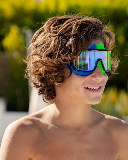 boy smiling poolside wearing prismatic swim goggles in cyborg cyan showing wide frame, neon colored gasket and mirrored lens