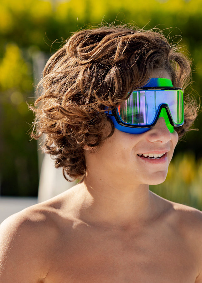boy smiling poolside wearing prismatic swim goggles in cyborg cyan showing wide frame, neon colored gasket and mirrored lens