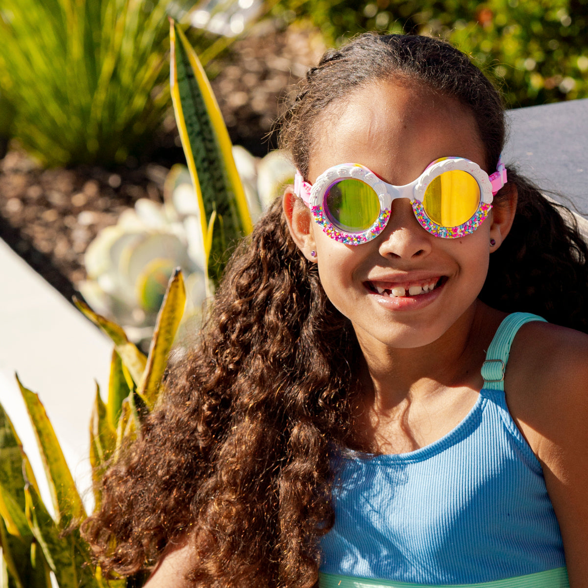 girl smiling poolside wearing bake off kids' round shaped swim goggles in color burst rainbow showing faux frosting detail and rainbow sprinkles