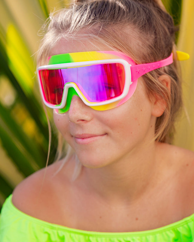 girl smiling poolside wearing chromatic kids swim goggles in multicolored melon showing a hot pink lens tint and melon colored swirl silicone gasket