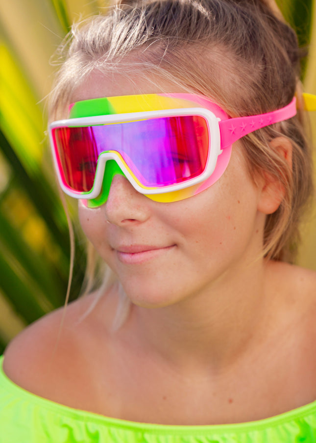 girl smiling poolside wearing chromatic kids swim goggles in multicolored melon showing a hot pink lens tint and melon colored swirl silicone gasket