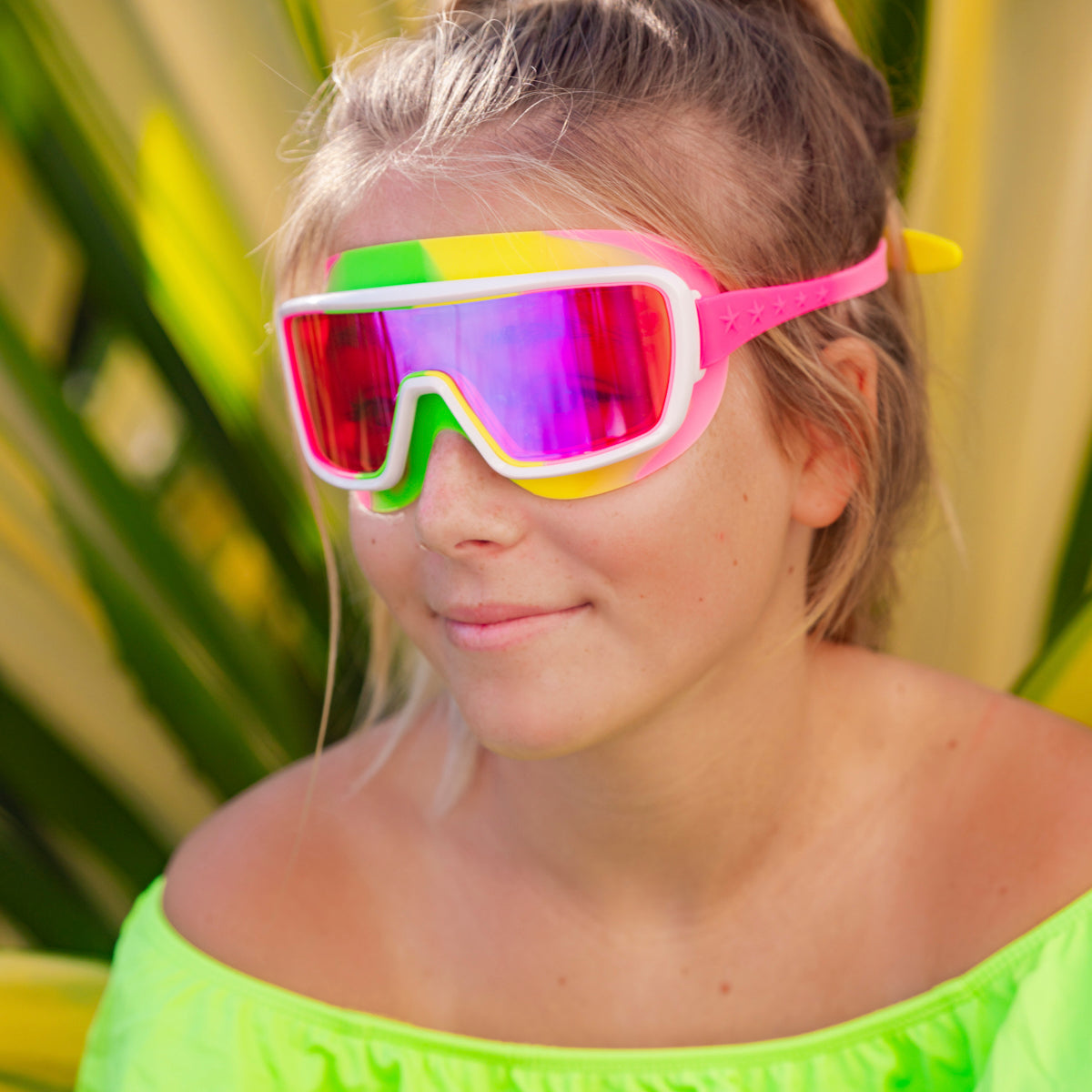 girl smiling poolside wearing chromatic kids swim goggles in multicolored melon showing a hot pink lens tint and melon colored swirl silicone gasket