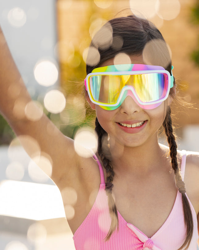 girl smiling and making a splash wearing chromatic kids swim goggles in pseudo swirl showing a softer rainbow silicone gasket, white frame and reflective lens