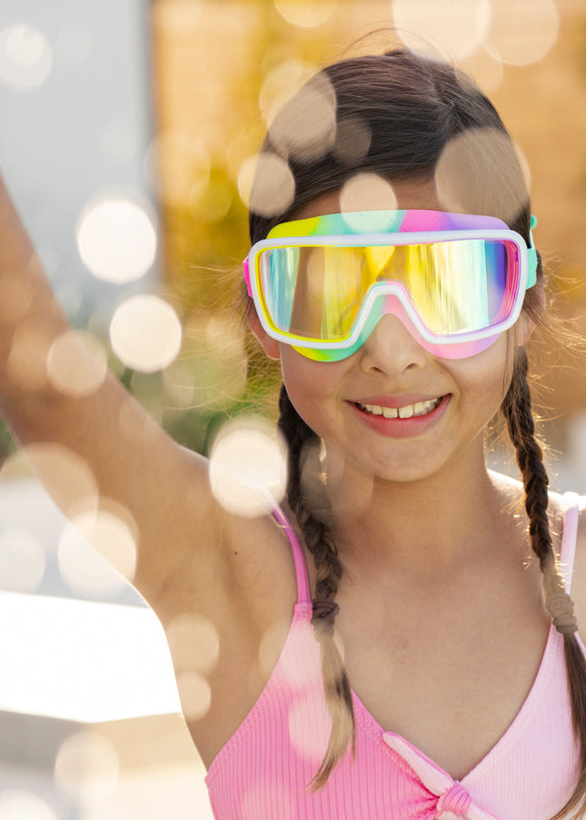 girl smiling and making a splash wearing chromatic kids swim goggles in pseudo swirl showing a softer rainbow silicone gasket, white frame and reflective lens
