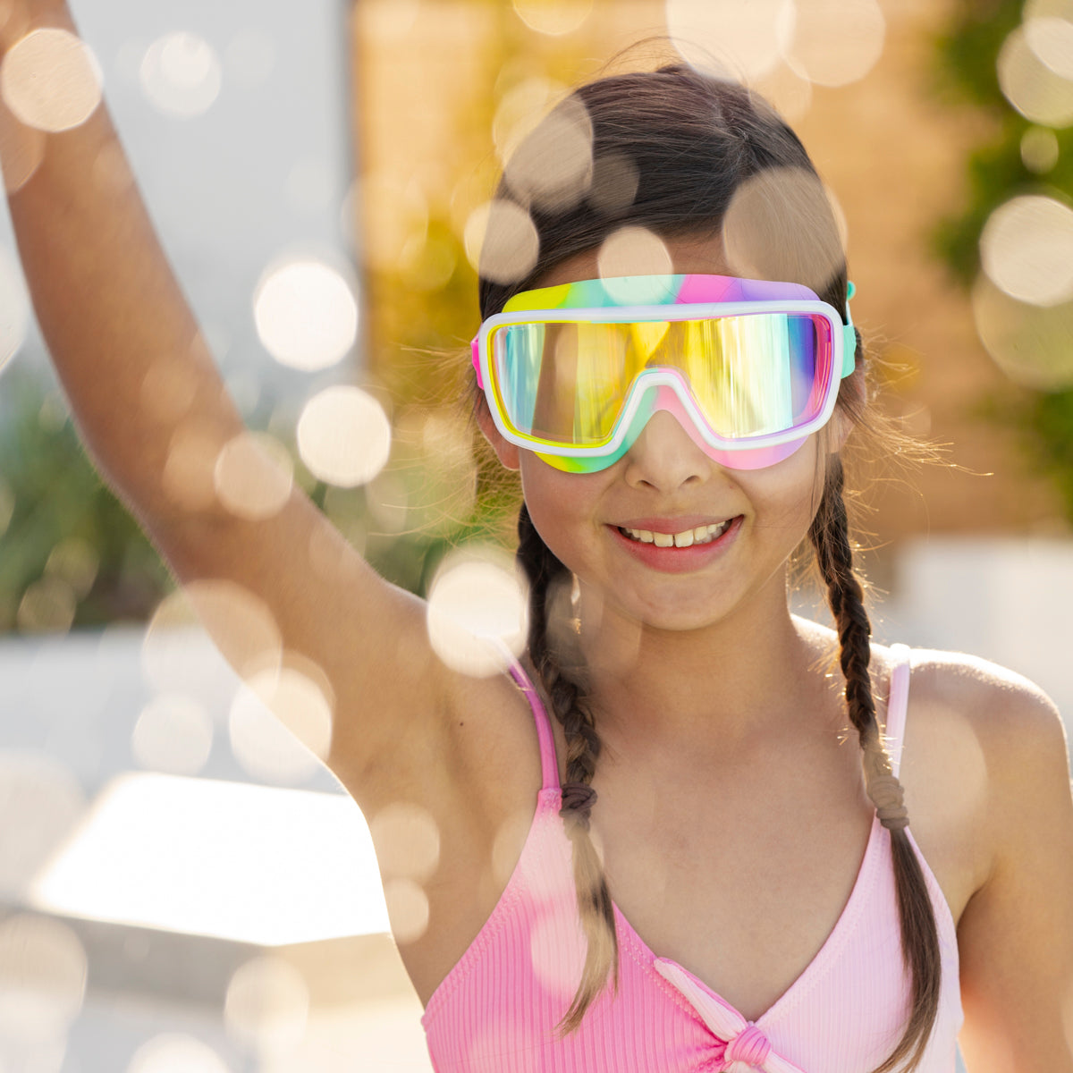 girl smiling and making a splash wearing chromatic kids swim goggles in pseudo swirl showing a softer rainbow silicone gasket, white frame and reflective lens