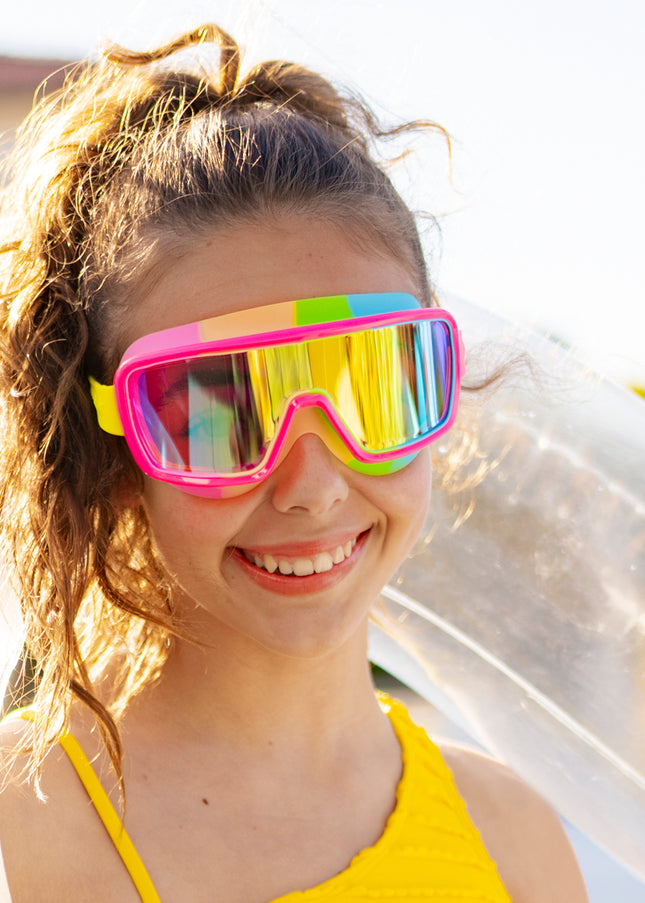girl smiling poolside wearing chromatic swim goggles in spectro strawberry showing a hot pink frame and rainbow colored gasket with reflective lens