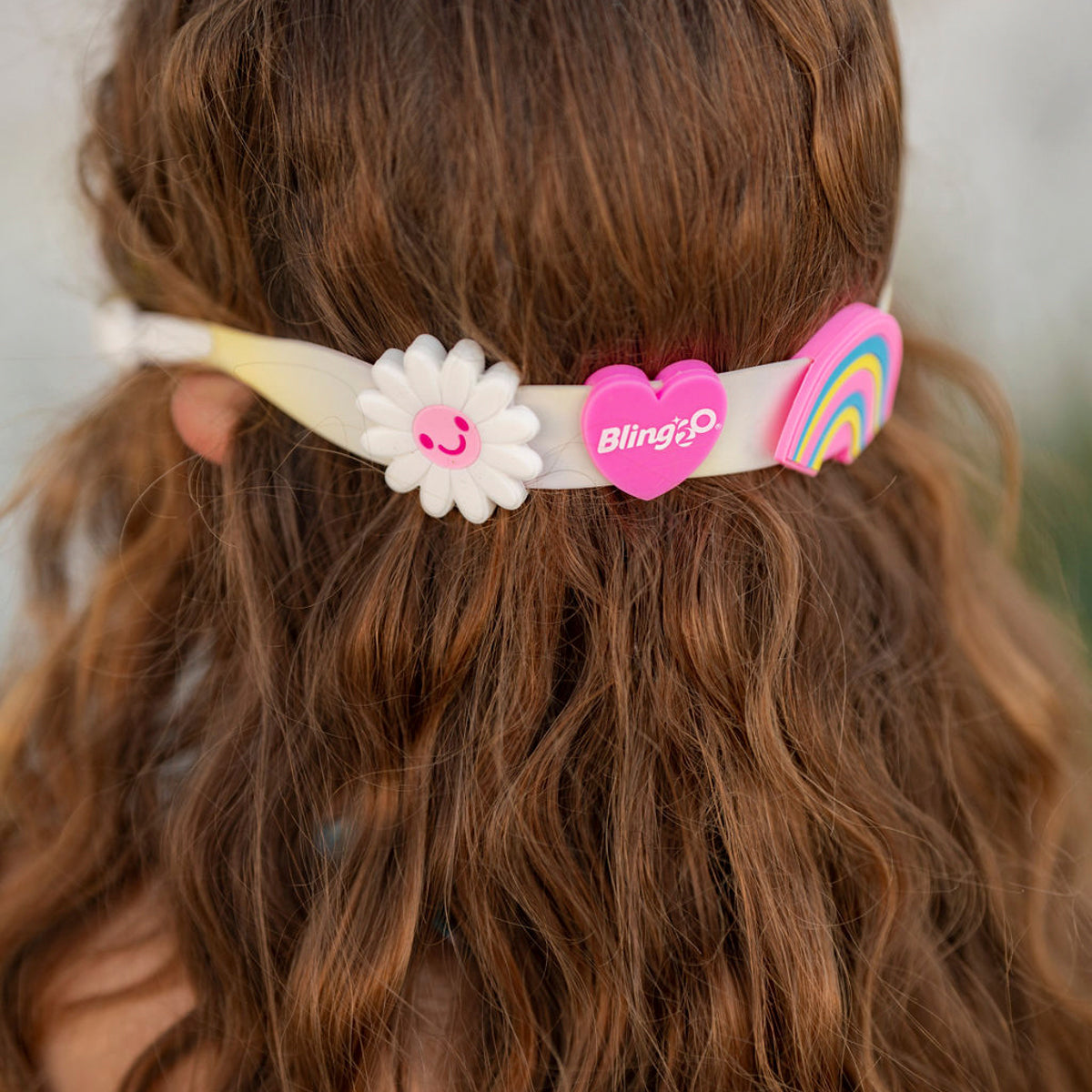 back of girls head wearing bright bouquet of daisies kids heart shaped swim goggles showing silicone daisy, heart, and rainbow sliders on the strap