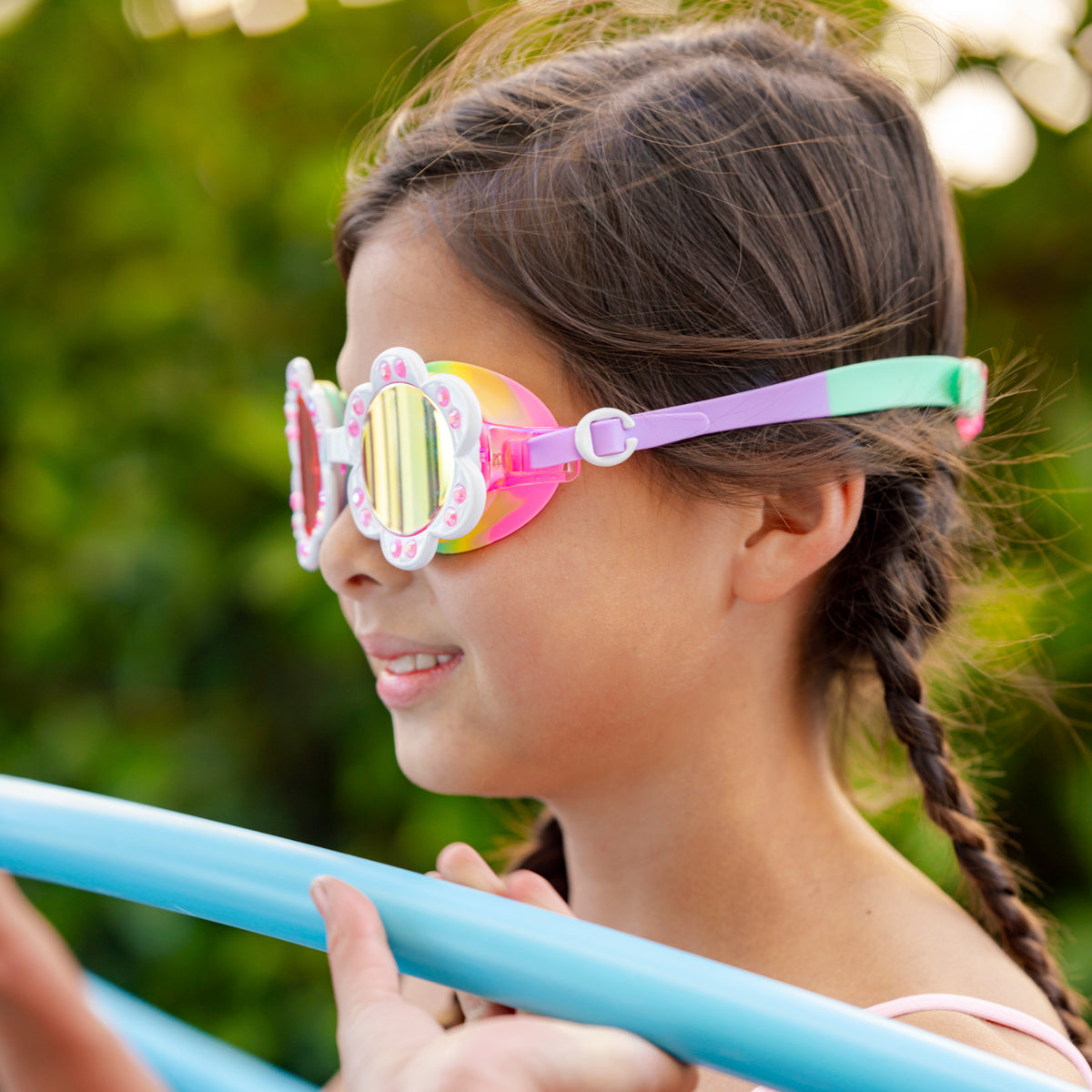 girl smiling playing poolside games wearing dandi flower shaped swim goggles in sunlit sherry showing petal detail with rhinestone and bright rainbow colored strap and gasket 