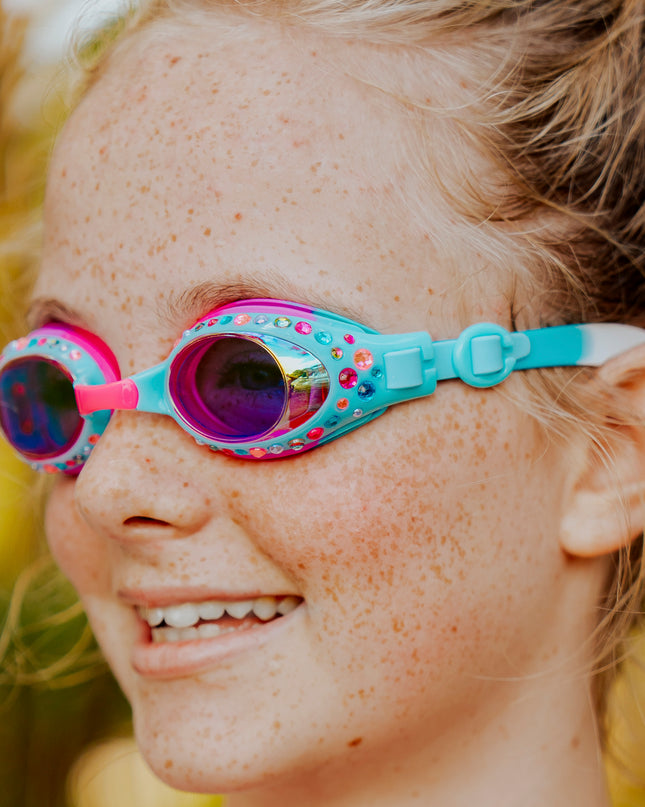close-up view of girl smiling wearing glimmering gemstones kids' swim goggles in crystal violet showing colorful rhinestones on a bright blue frame