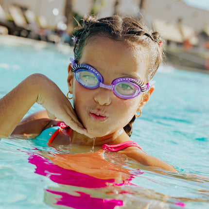 girl in swimming pool posing wearing splash lash kids' swim goggles in purple polish showing faux lashes and rhinestones