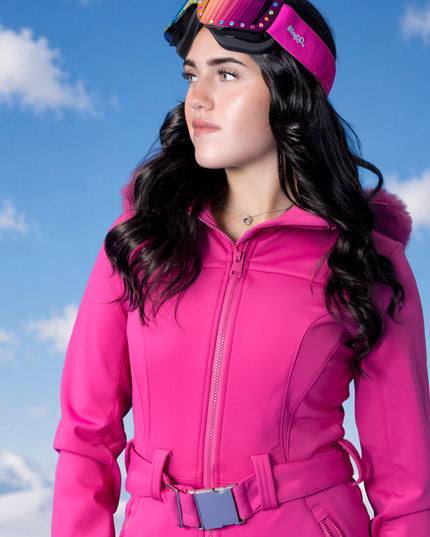 woman standing with blue sky background in pink ski suit wearing powder pop ski goggles in alpen glow