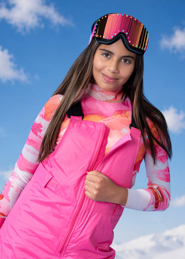 girl standing in pink snow suit smiling wearing powder pop kids ski goggles in pink aura showing a pink mirrored lens with rainbow rhinestones around the frame