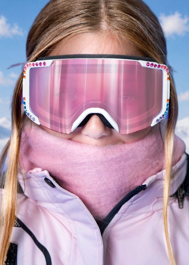 headshot of model wearing pink scarf and jacket matching pink powder pop kids' ski goggles in prism powder showing pink mirrored lens and rainbow rhinestones around white frame