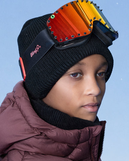 boy wearing prism peak kids' ski goggles featuring a red orange mirrored lens with black spikes and a monster eye decal with a black strap and red buckle