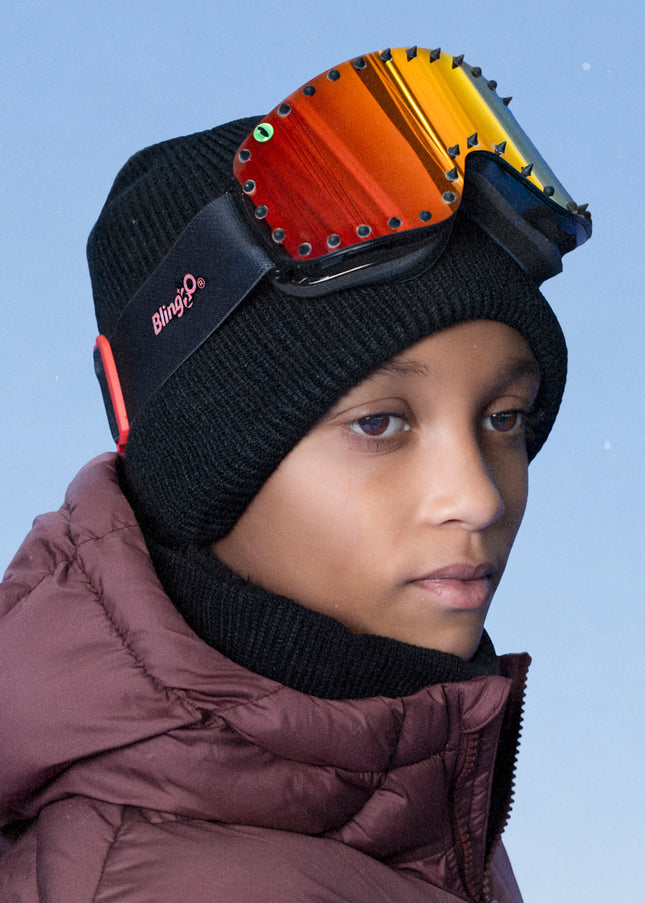 boy wearing prism peak kids' ski goggles featuring a red orange mirrored lens with black spikes and a monster eye decal with a black strap and red buckle