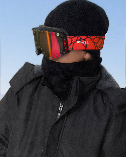 boy wearing prism peak kids' ski goggles featuring a red orange mirrored lens with black spikes and a monster eye decal with a black strap and red buckle