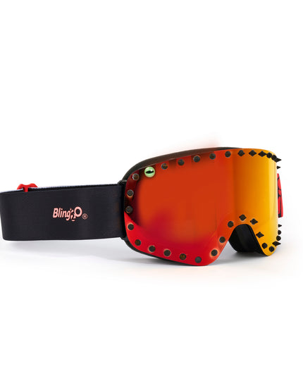 side angle of prism peak kids' ski goggles featuring a red orange mirrored lens with black spikes and a monster eye decal with a black strap and red buckle