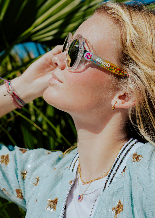girl posing in sun smiling wearing glass beach kids sunglasses in sprinkle sunrise showing clear large round frame with 3D gumballs in the arm of the sunglass