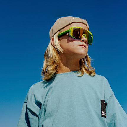 child at beach looking off wearing gulf shore kids' sunglasses in gator glare green showing gator textured arms and frame
