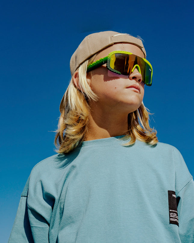 child at beach looking off wearing gulf shore kids' sunglasses in gator glare green showing gator textured arms and frame