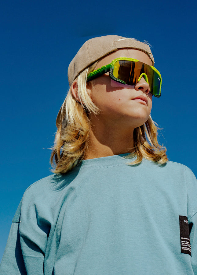 child at beach looking off wearing gulf shore kids' sunglasses in gator glare green showing gator textured arms and frame