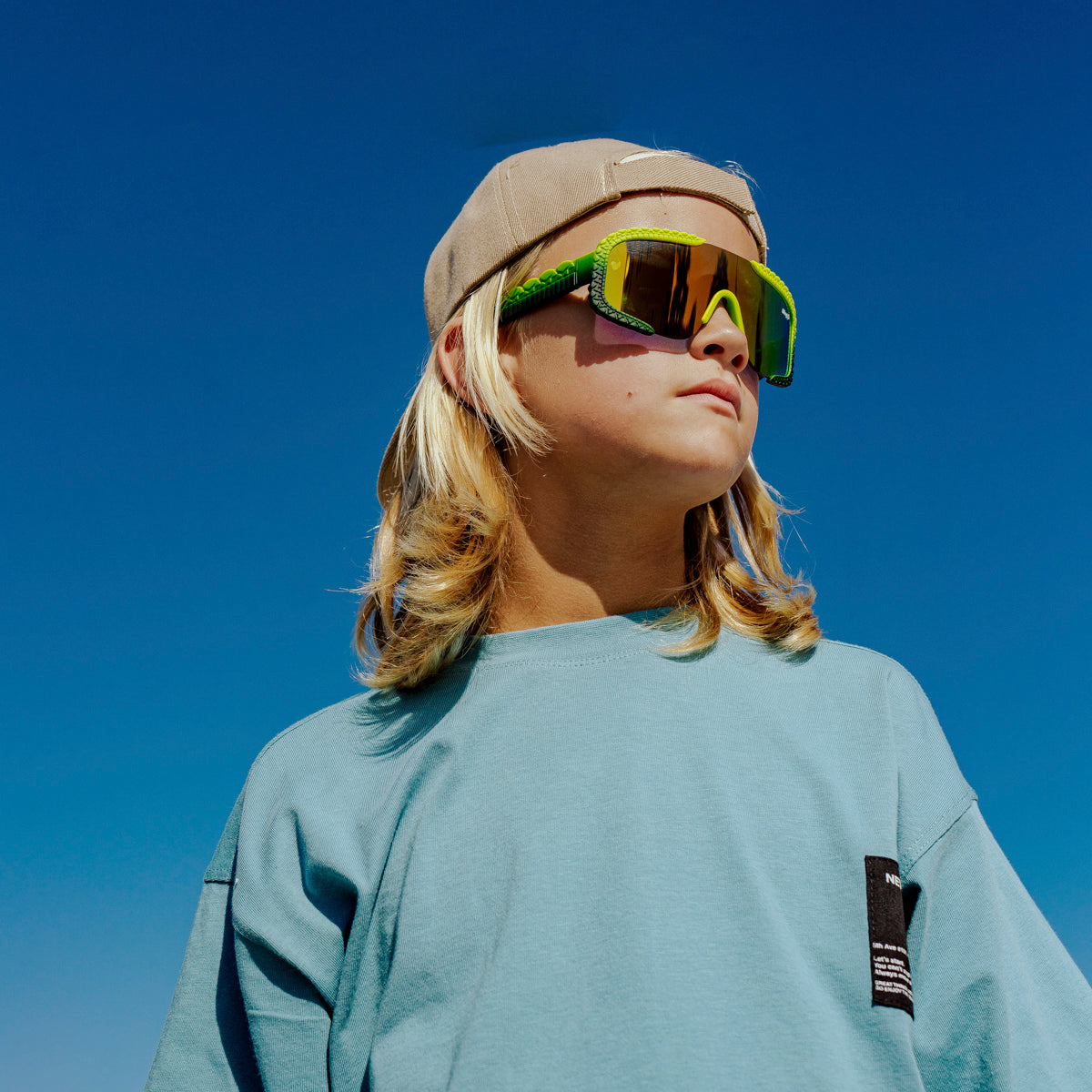 child at beach looking off wearing gulf shore kids' sunglasses in gator glare green showing gator textured arms and frame