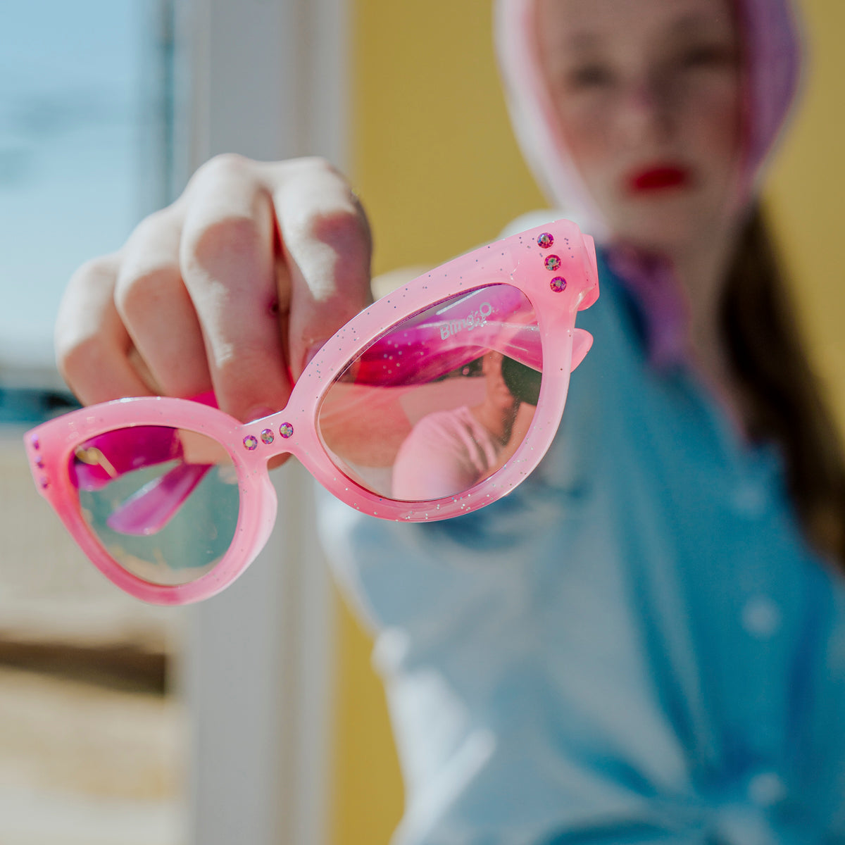 girl holding malibu beach kid's sunglasses in pisces pink to camera showing pink glitter frame and pink rhinestone detail