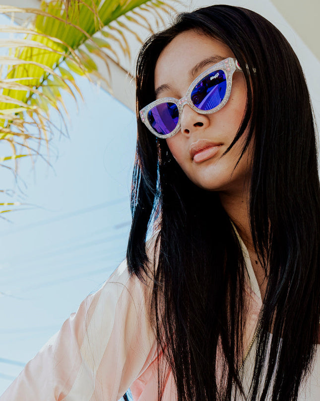 girl posing in sunlight and palm trees wearing malibu beach kids' sunglasses in starship sparkle showing a silver glitter infused frame and pink rhinestones