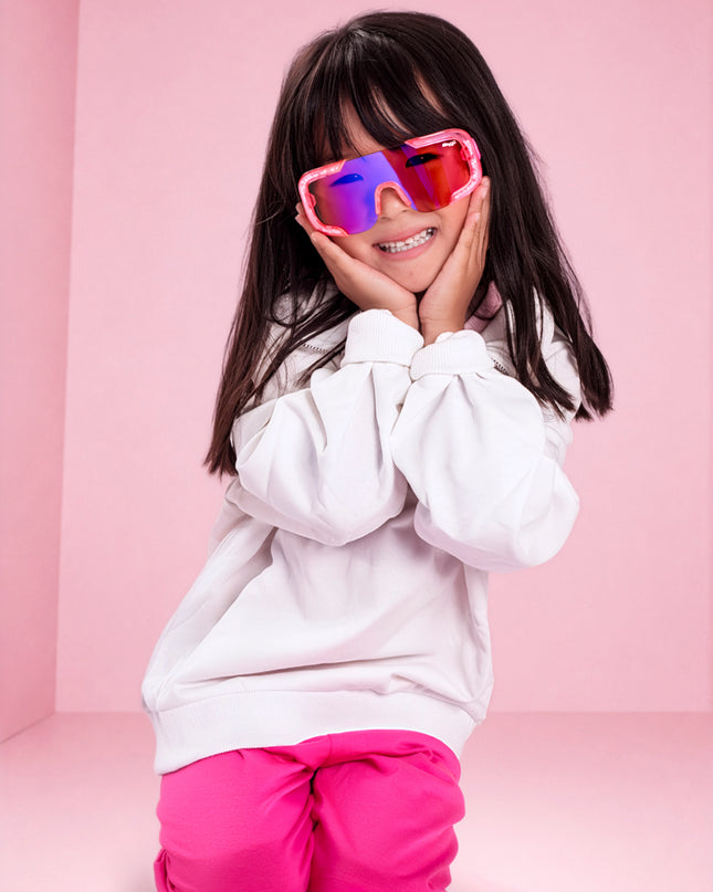 girl smiling in pink studio wearing pink sand kids sunglasses in the color sprinkle pink 