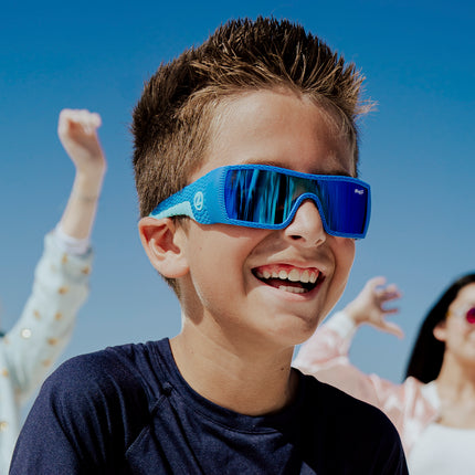 young boy smiling wearing sand harbor kids' sunglasses in sky blue stegosaur showing a sleek frame and dino textured arm of sunglass