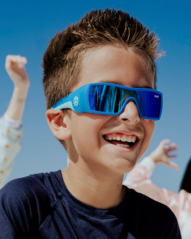 young boy smiling wearing sand harbor kids' sunglasses in sky blue stegosaur showing a sleek frame and dino textured arm of sunglass