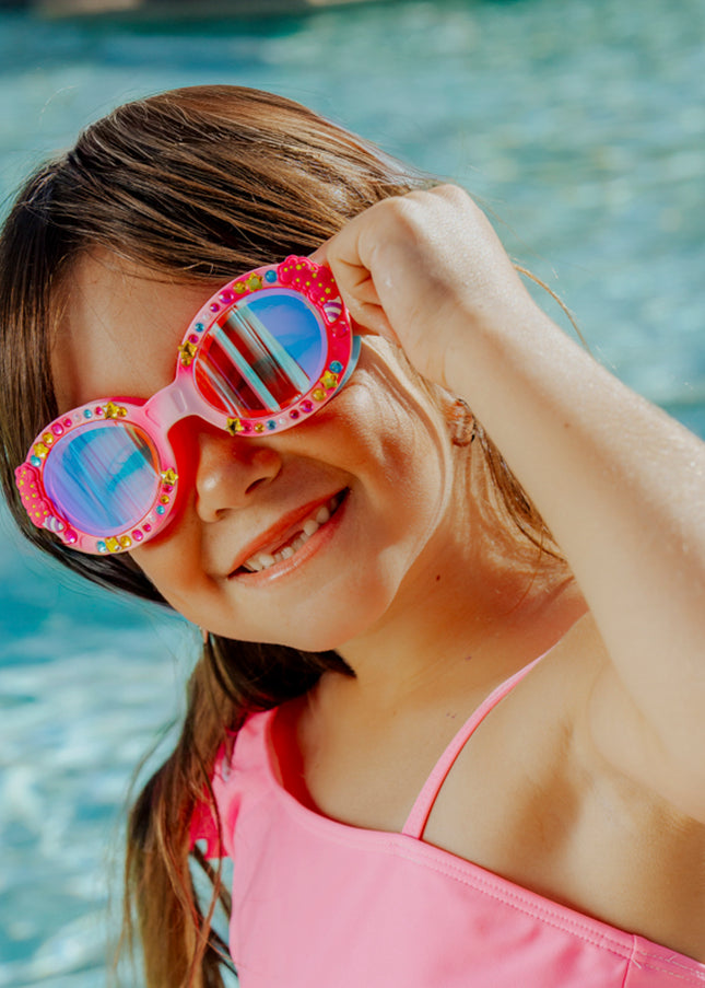 lifestyle of girl in front of pool smiling wearing candy carnival kids swim goggles showing rhinestones and cotton candy detail