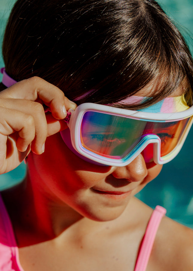 lifestyle of girl in front of swimming pool wearing cyberswim kids' swim goggles in robo rainbow 