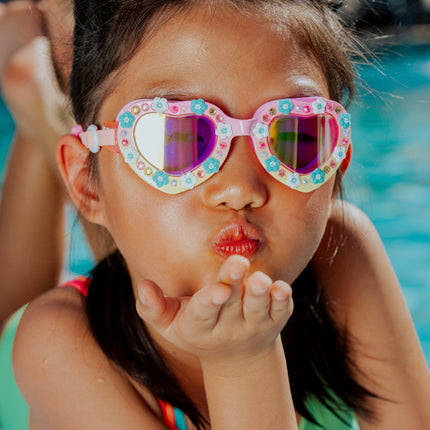 lifestyle of girl playfully blowing kiss poolside wearing daisies at dawn heart shaped swim goggles