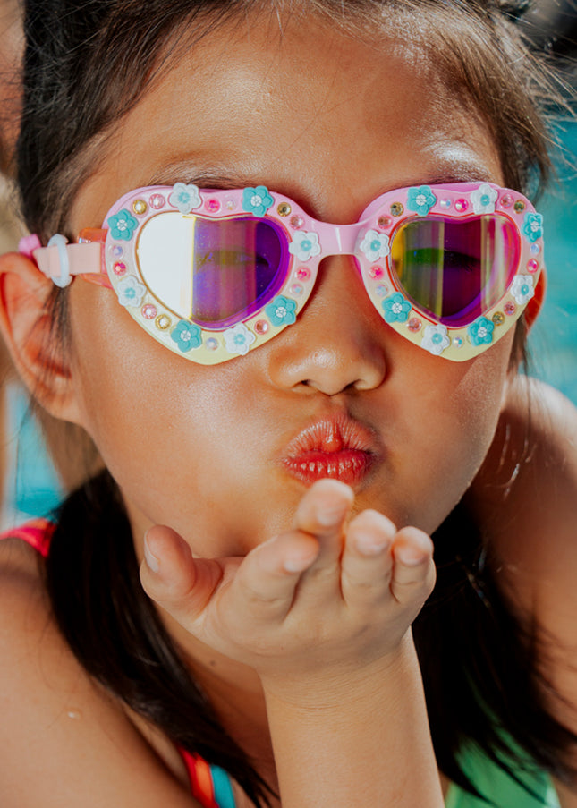 lifestyle of girl playfully blowing kiss poolside wearing daisies at dawn heart shaped swim goggles
