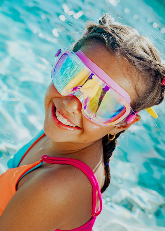 lifestyle of girl sitting poolside wearing hologlow swim goggles in bubblegum beam pink showing reflective lens