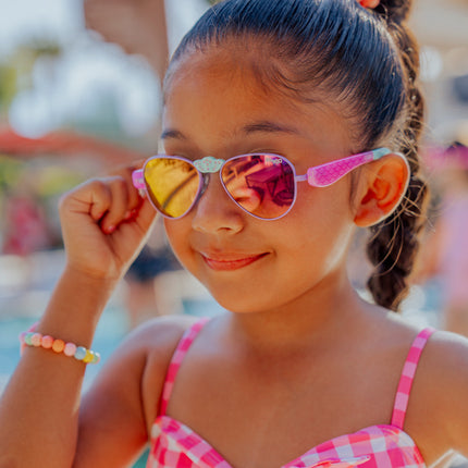 lifestyle of girl smiling adjusting hampton kids sunglasses in suntan turq showing mermaid tail detail on arm and rhinestone nose piece
