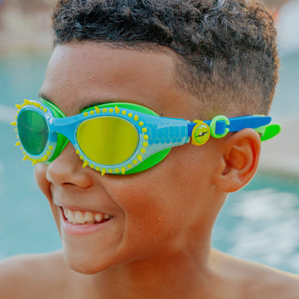 lifestyle of kid smiling wearing jurassic dive swim goggles in stego splash green showing silicone spike details and reptilian printed lens with eye ball slider detail