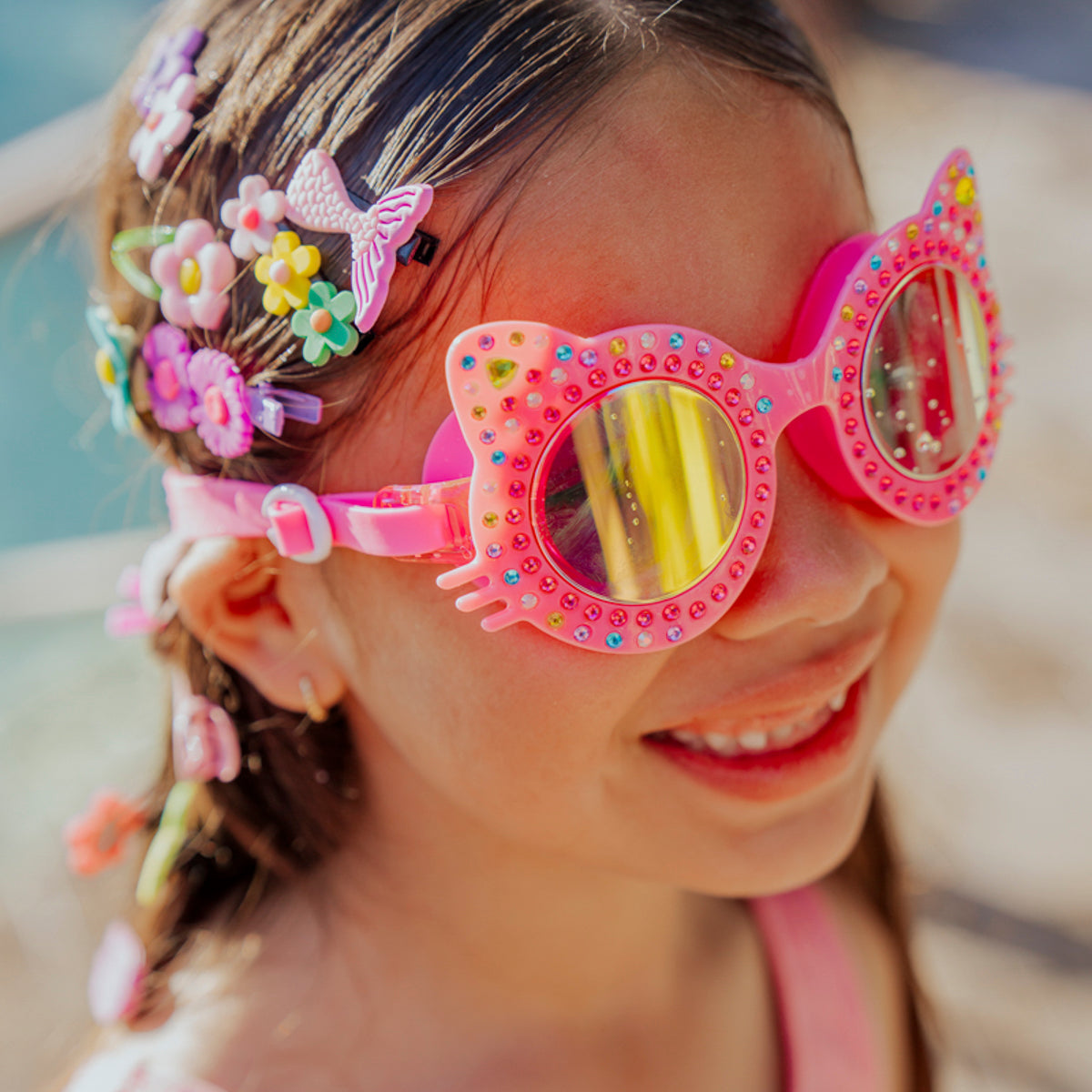 lifestyle of girl smiling in bedazzled accessories wearing Kitten kids swim goggles in mango mittens hot pink cat shaped swim goggles 