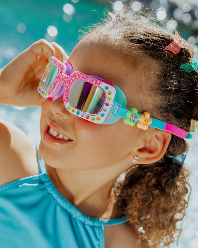 angled Lifestyle of 4 year old girl smiling wearing Pretty Girl Poppy in Petal Pop Pink kids' swim goggles showing silicone flower sliders