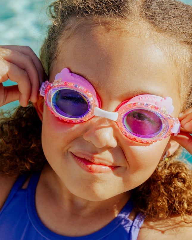 lifestyle of girl wearing rainbow swim goggles in floating fuchsia showing rhinestones and rainbow shaped silicone gasket