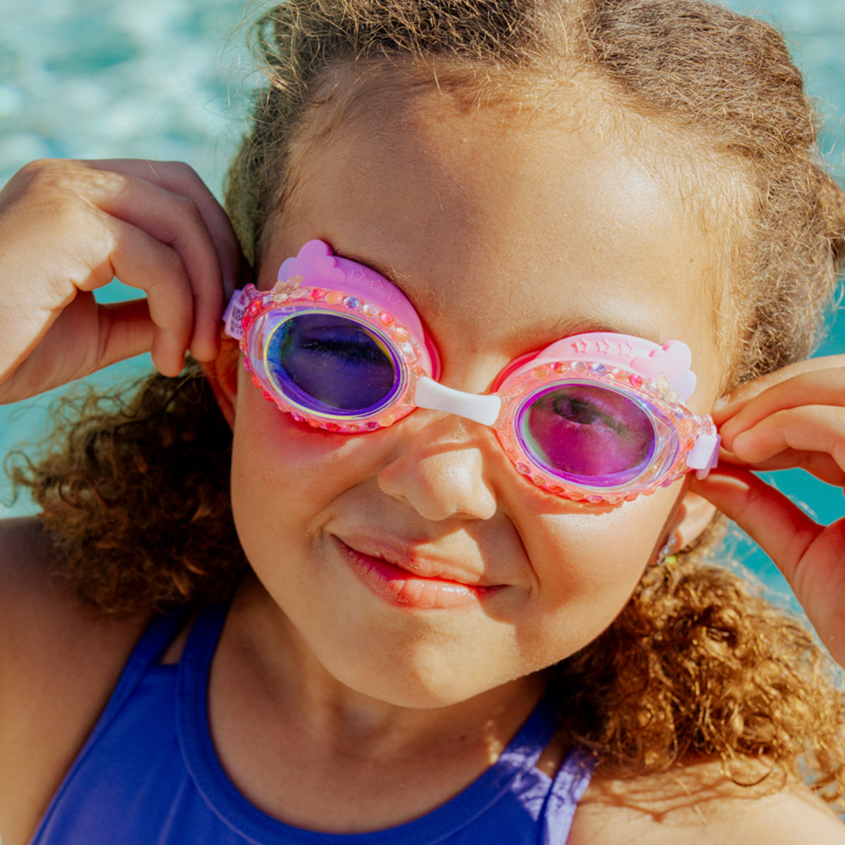 lifestyle of girl wearing rainbow swim goggles in floating fuchsia showing rhinestones and rainbow shaped silicone gasket