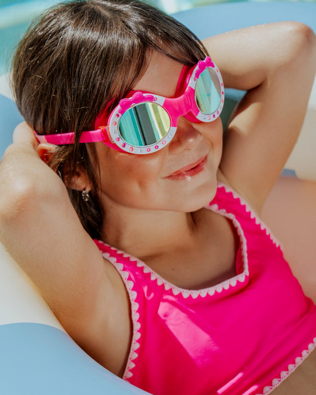 lifestyle image of girl wearing ribbon glam kids swim goggles laying in inflatable inner tube
