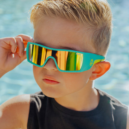 boy wearing sand harbor kids sunglasses in teal triceratops showing dino textured frame and reflective lens