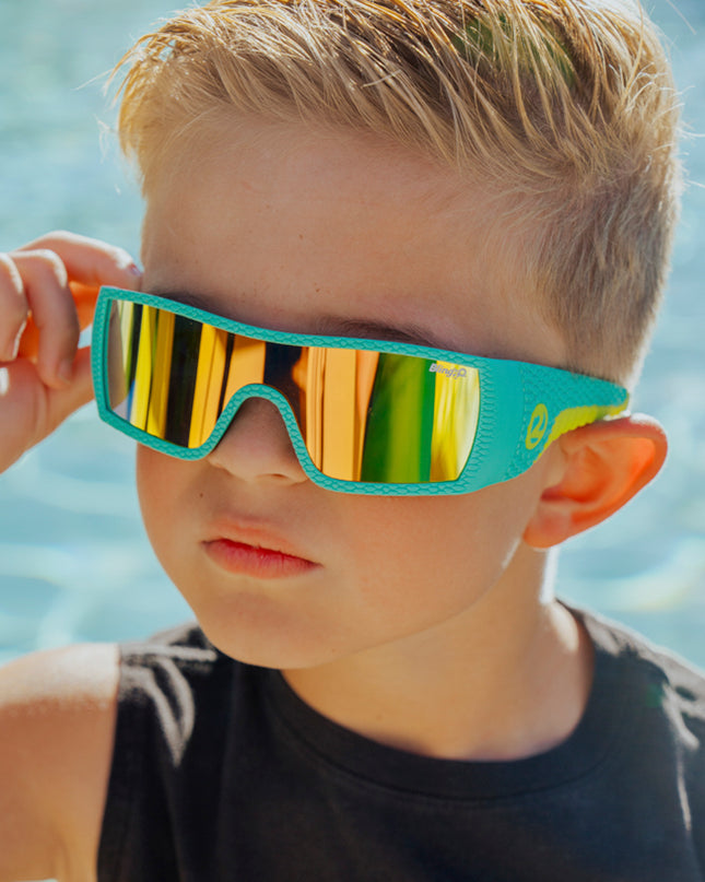 boy wearing sand harbor kids sunglasses in teal triceratops showing dino textured frame and reflective lens