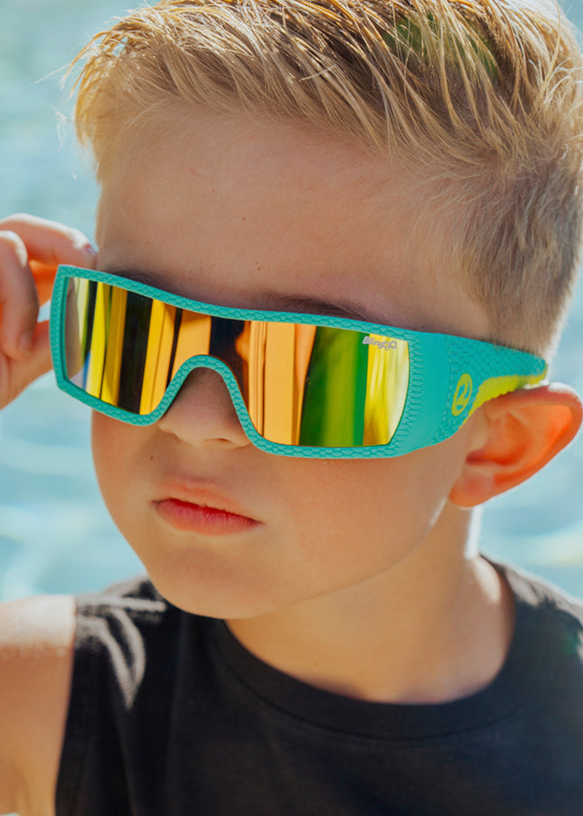 boy wearing sand harbor kids sunglasses in teal triceratops showing dino textured frame and reflective lens