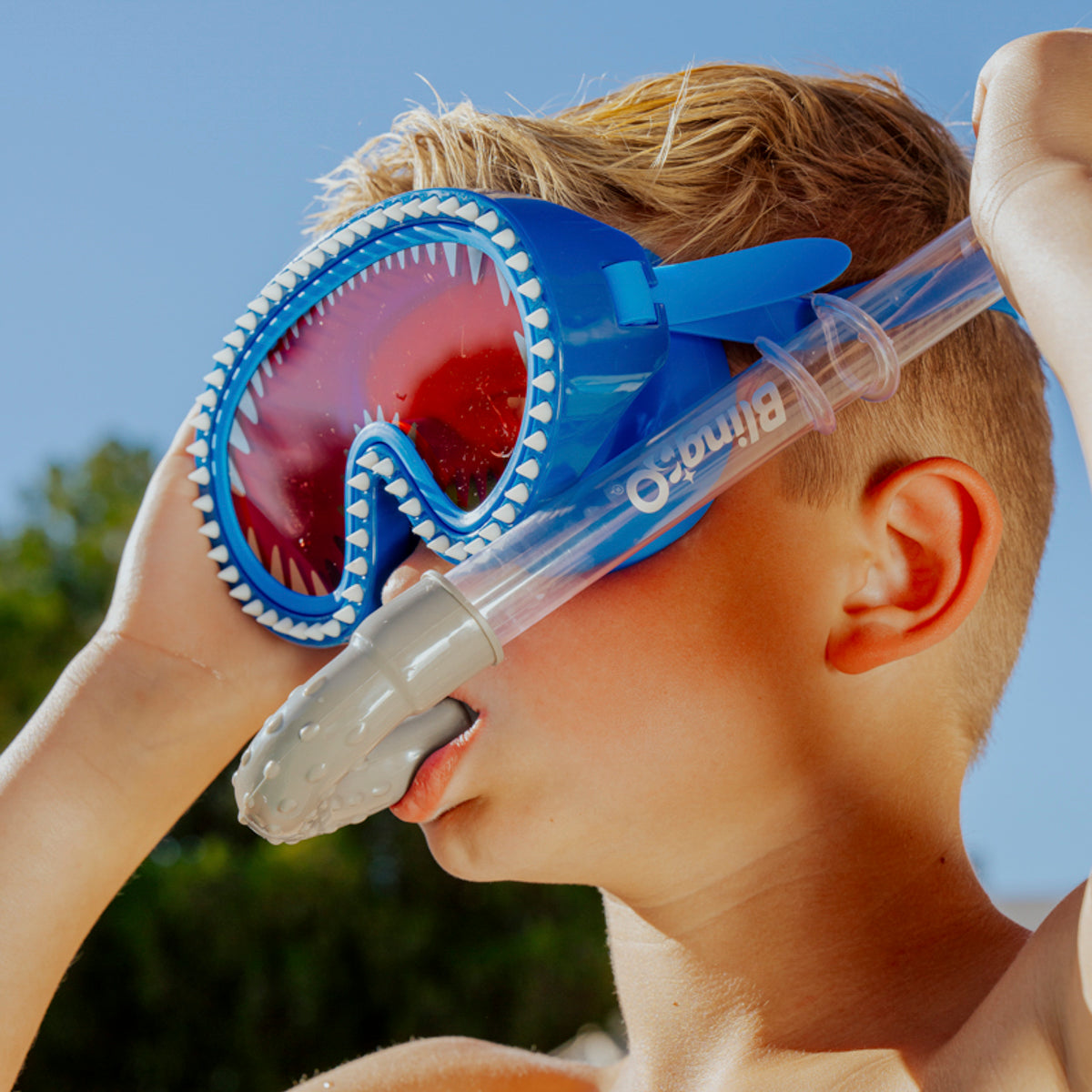angled view of boy wearing shark attack kids swim mask showing silicone spike details and red lens while using shark bite shark fin snorkel in blue grey 