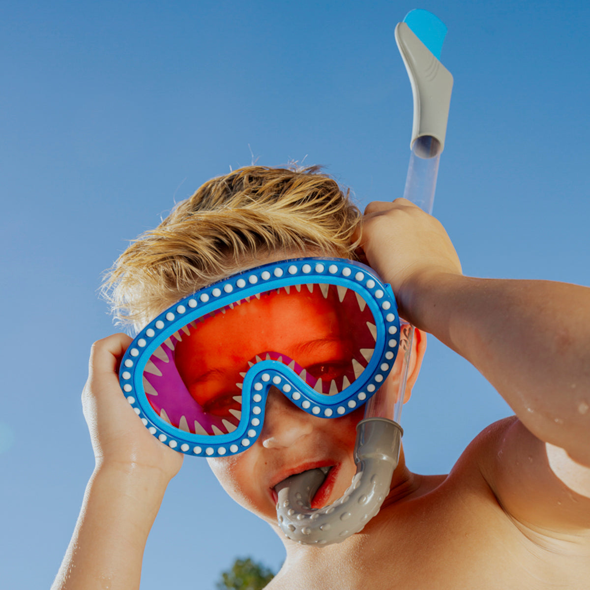 boy wearing shark attack kids swim mask showing silicone spike details and red lens while using shark bite shark fin snorkel in blue grey 