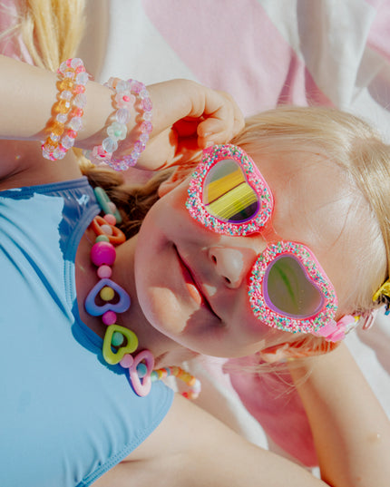 lifestyle image of child laying on beach towel wearing sprinkle heart kid's swim goggles 